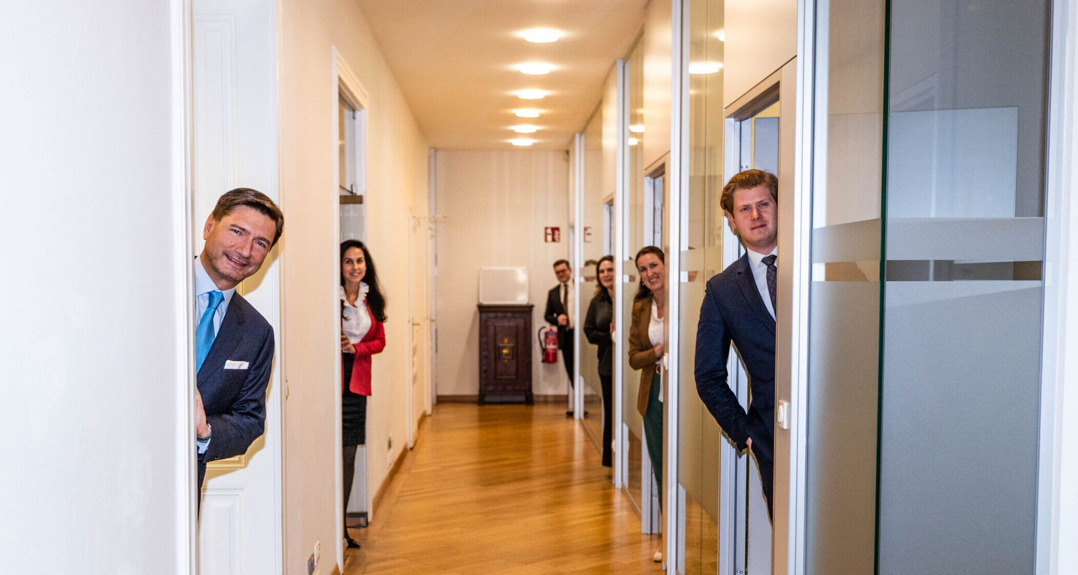 Teamfoto im Flur, Mitarbeiter schauen aus Ihren Büros heraus in die Kamera Teamfoto im Flur, Mitarbeiter schauen aus Ihren Büros heraus in die Kamera